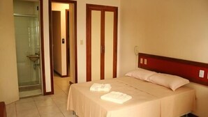 Quarto de hotel com uma cama, chuveiro e porta que dá para outro quarto.
