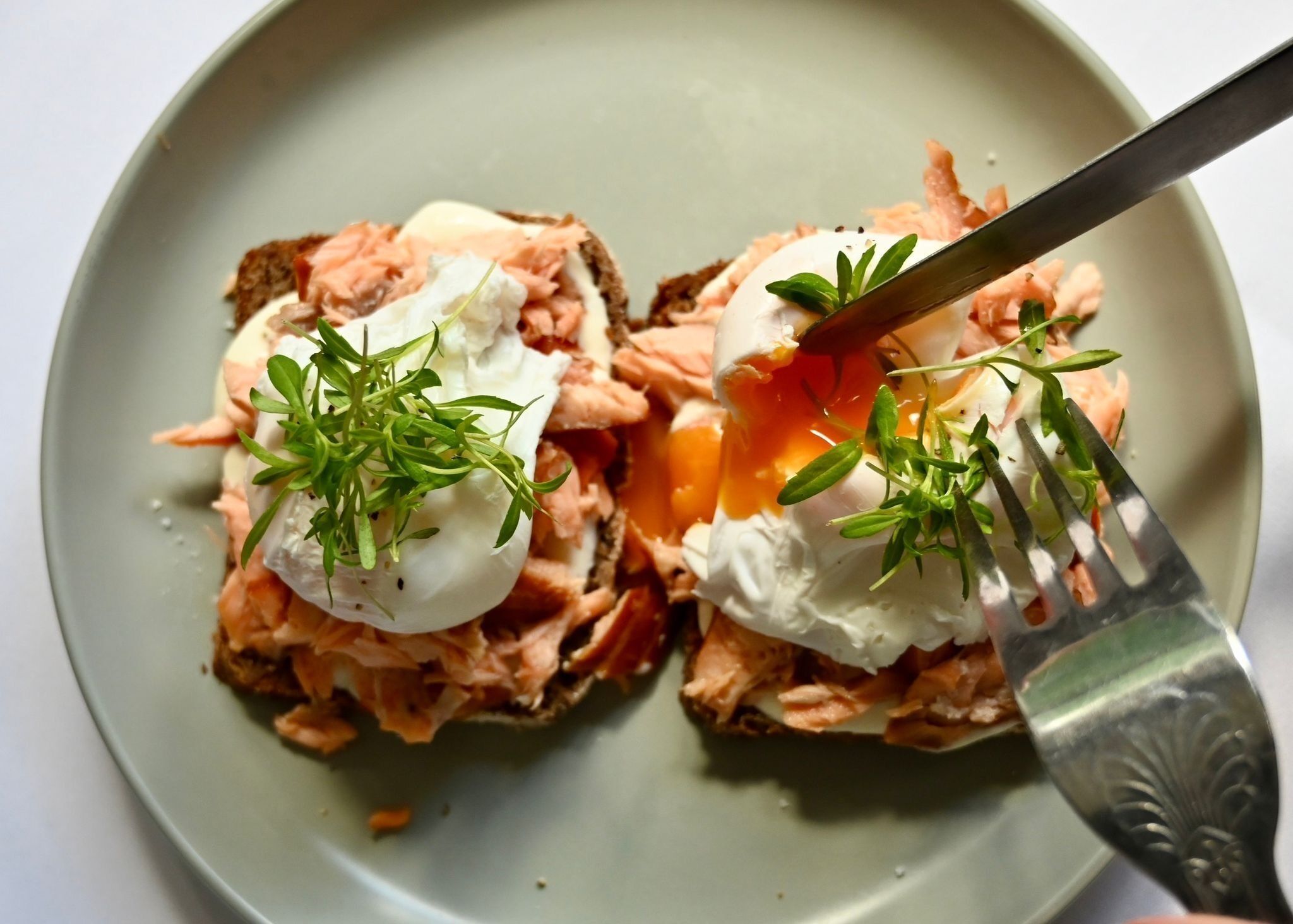 A plate with two open-faced sandwiches topped with poached eggs and fresh herbs.