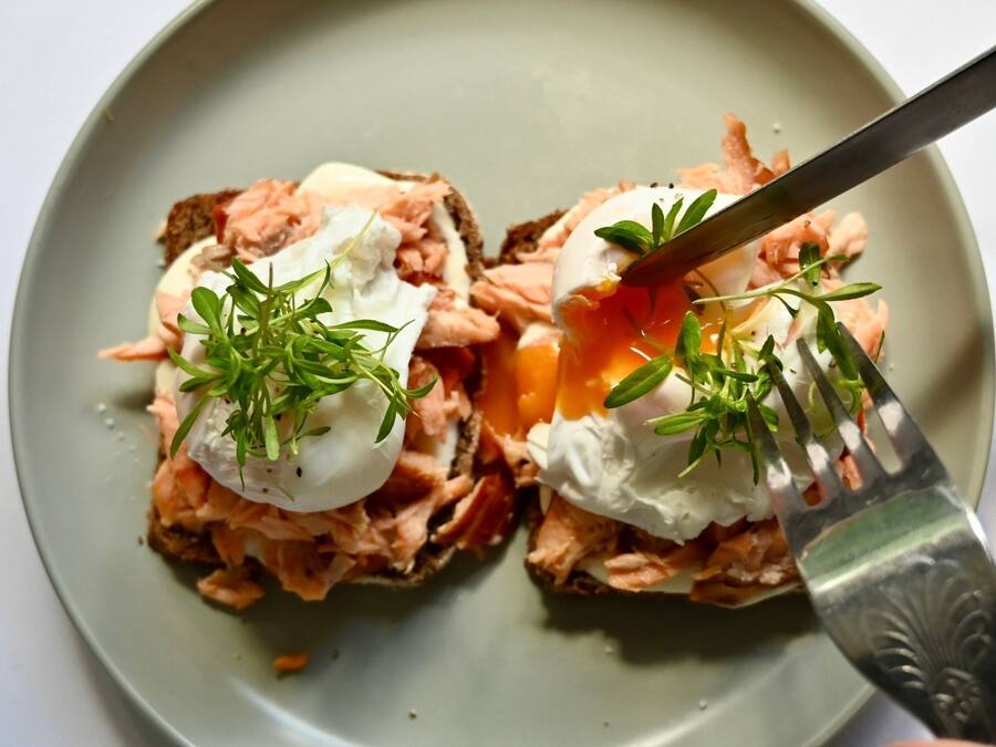 A plate with two open-faced sandwiches topped with poached eggs and fresh herbs.