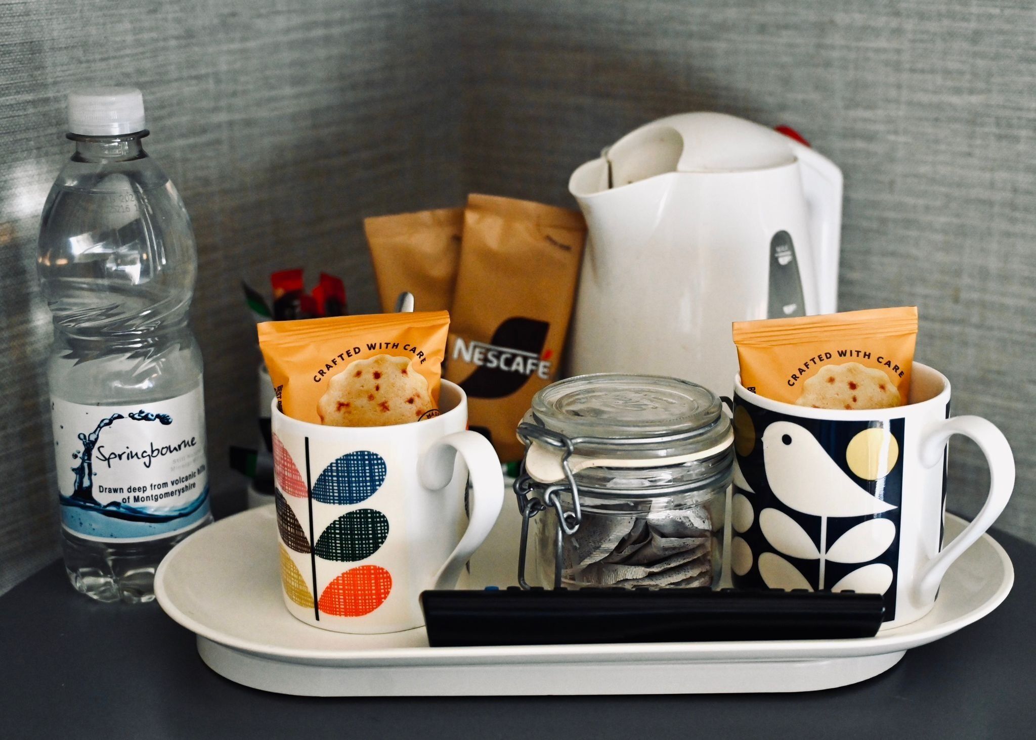 A tray with two mugs, a water bottle, a jar, and a Nescafe bag.