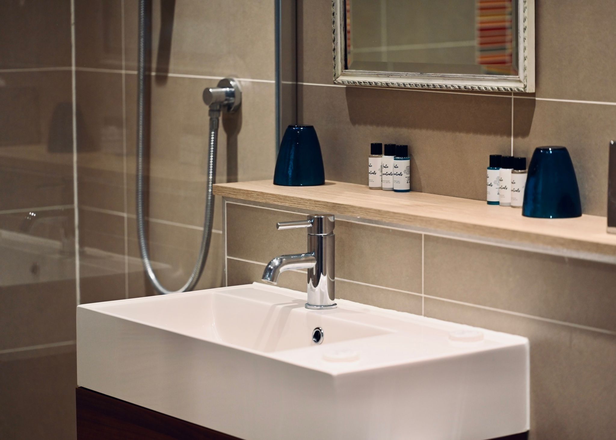 Un baño moderno con un lavabo blanco, un cabezal de ducha de mano y un estante con artículos de aseo.