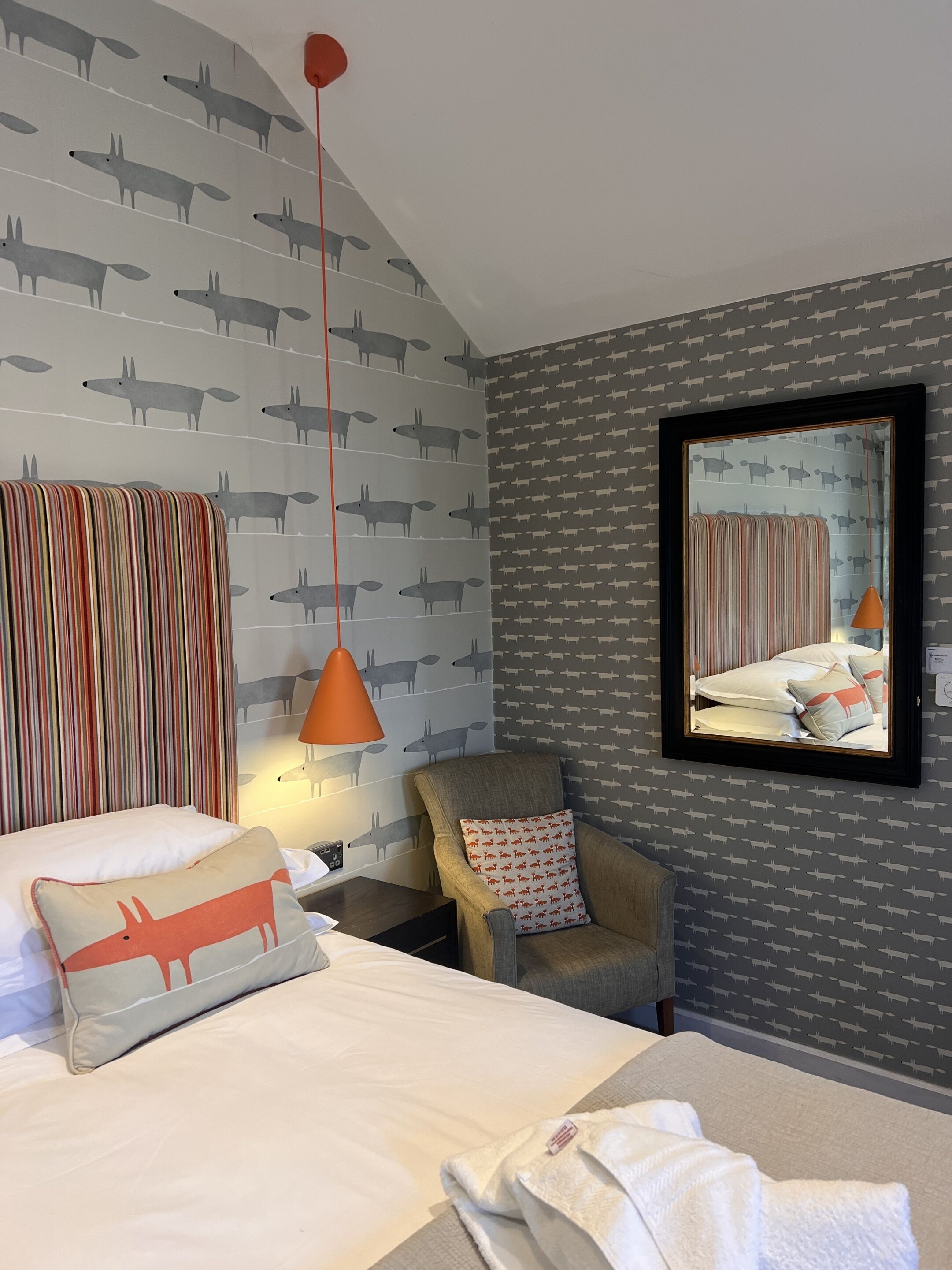 A hotel room with a bed, a chair, a nightstand, a lamp, and a mirror.