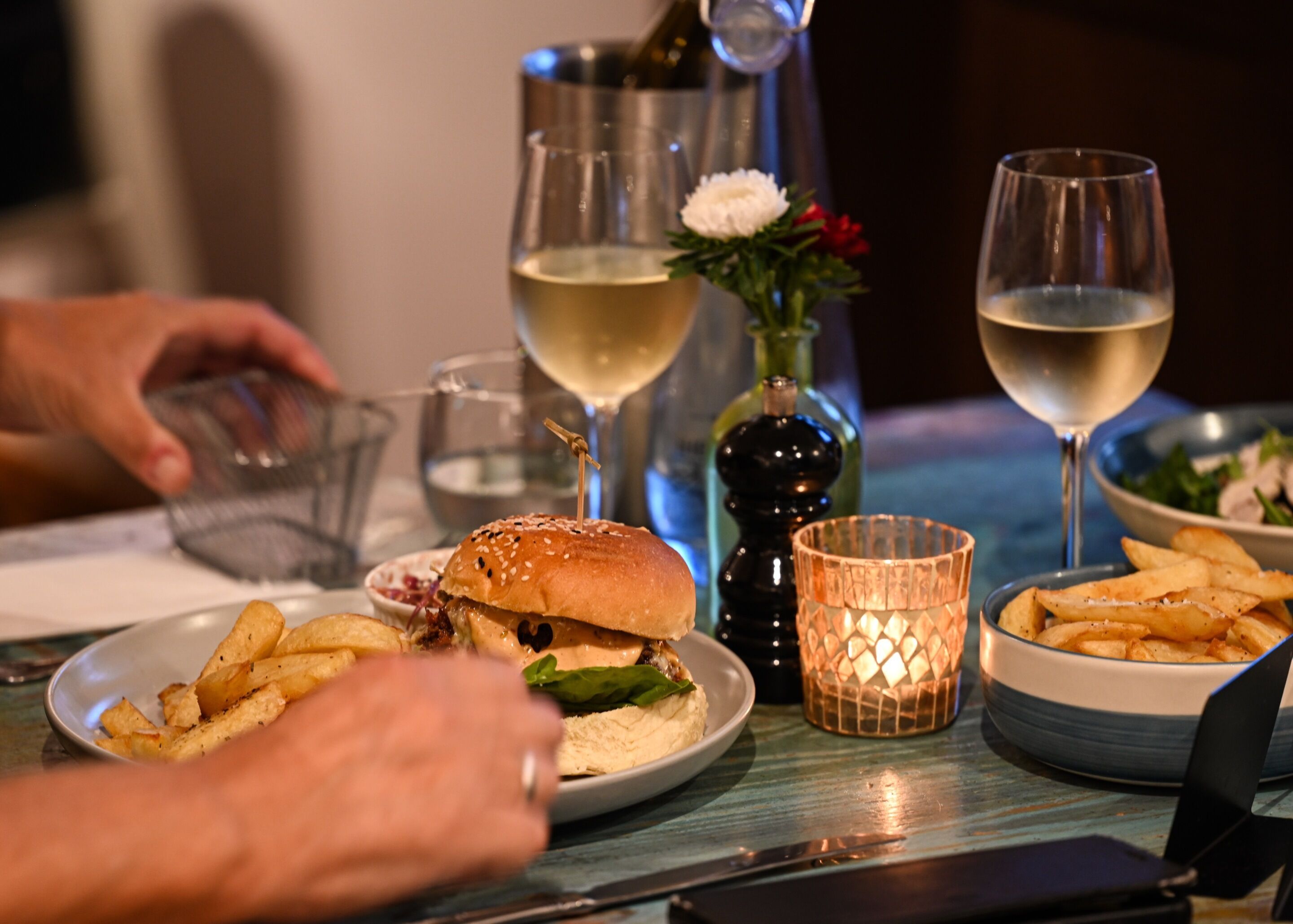 Una mesa de comedor con una hamburguesa, papas fritas y una botella de vino.