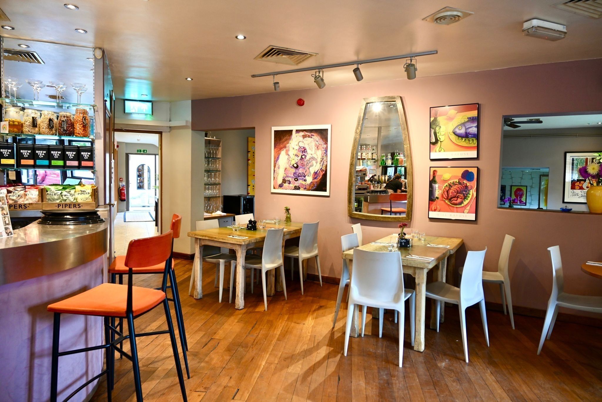 Interior de restaurante com área de bar, mesas para refeições, cadeiras e diversos itens de comida e bebida em exposição.