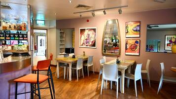 Interior de restaurante com área de bar, mesas para refeições, cadeiras e diversos itens de comida e bebida em exposição.