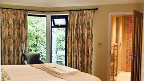Ein Schlafzimmer mit einem großen Bett, einem Sessel, einer Chandelüster und Blick auf Grünfläche.
