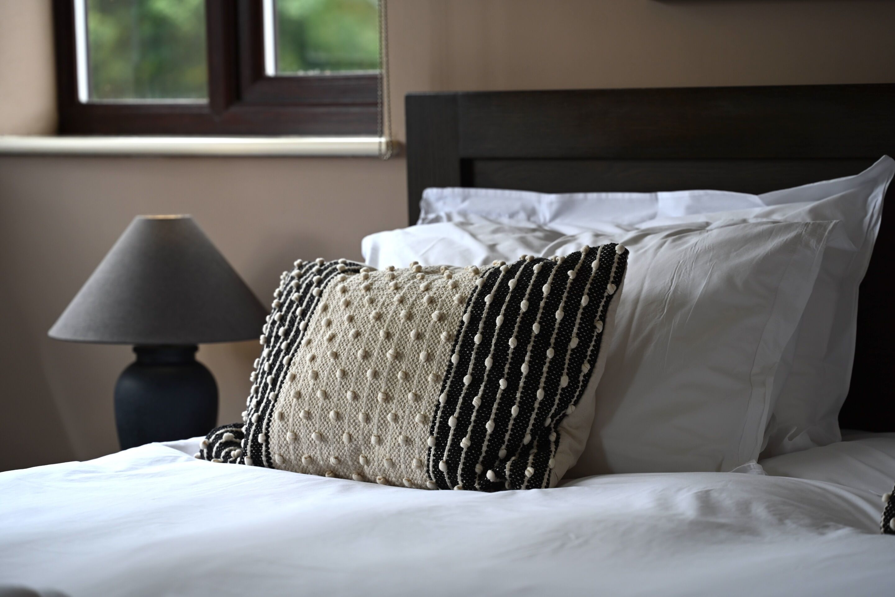 A neatly made bed with white linens and a decorative pillow.