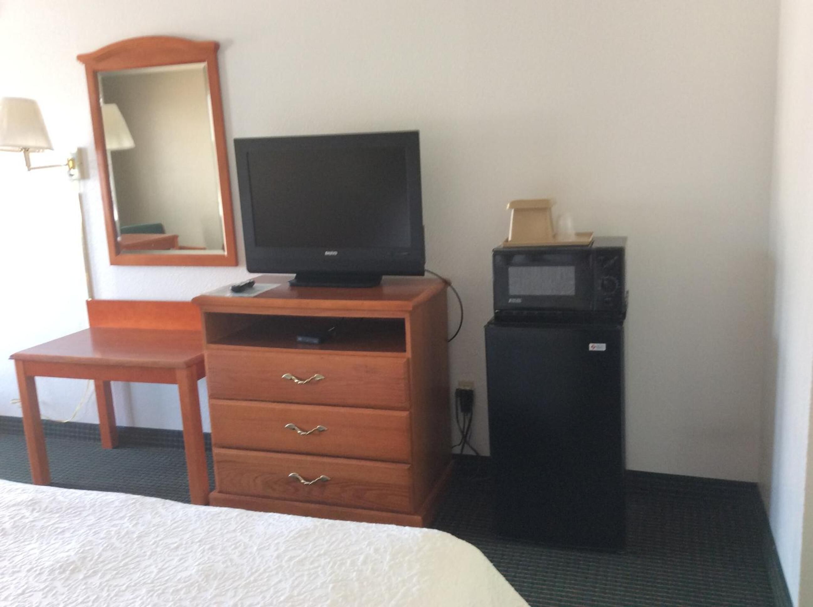 A hotel room with a wooden desk, a television, a microwave, and a bed.