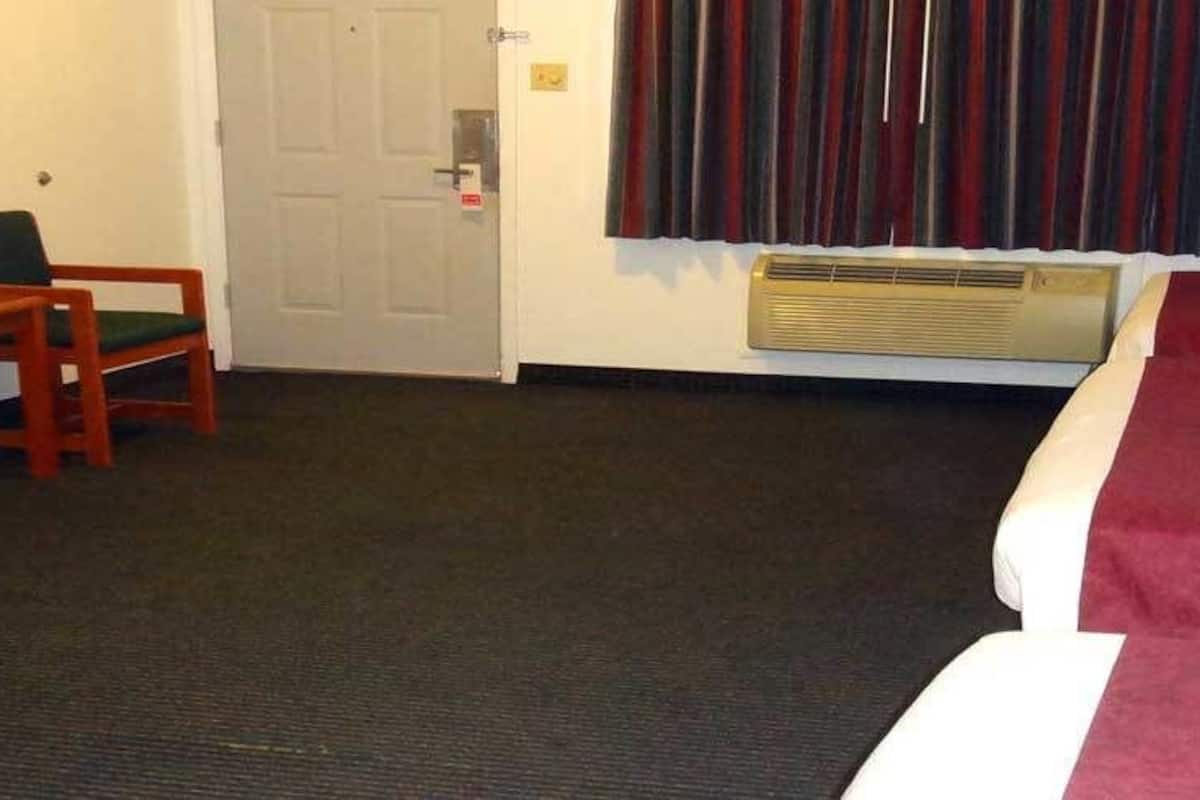 A hotel room with a bed, a desk with a chair, a television, and a window with curtains.