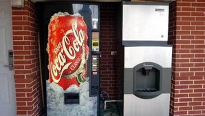 Una máquina expendedora con el logotipo de Coca-Cola Classic, una ranura para monedas y un área de dispensación de bebidas.