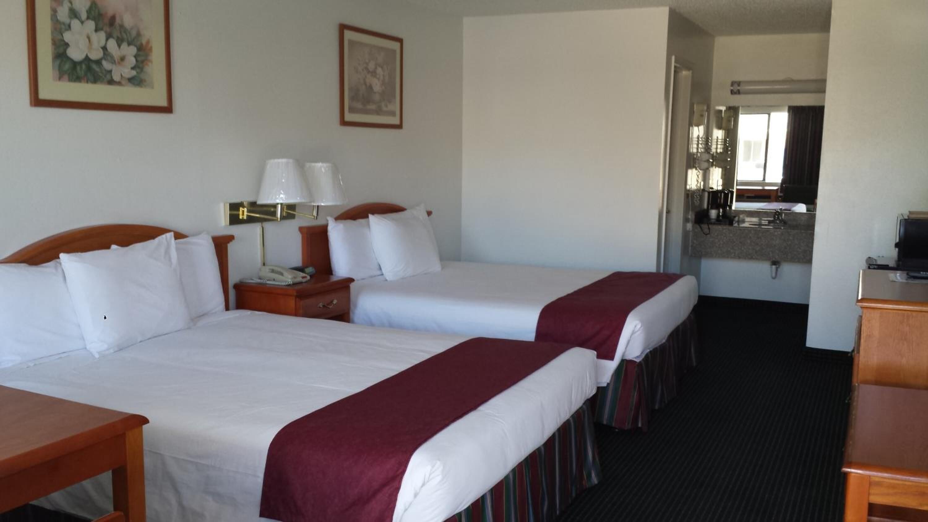 Quarto de hotel com duas camas, uma escrivaninha, telefone e uma mesinha.