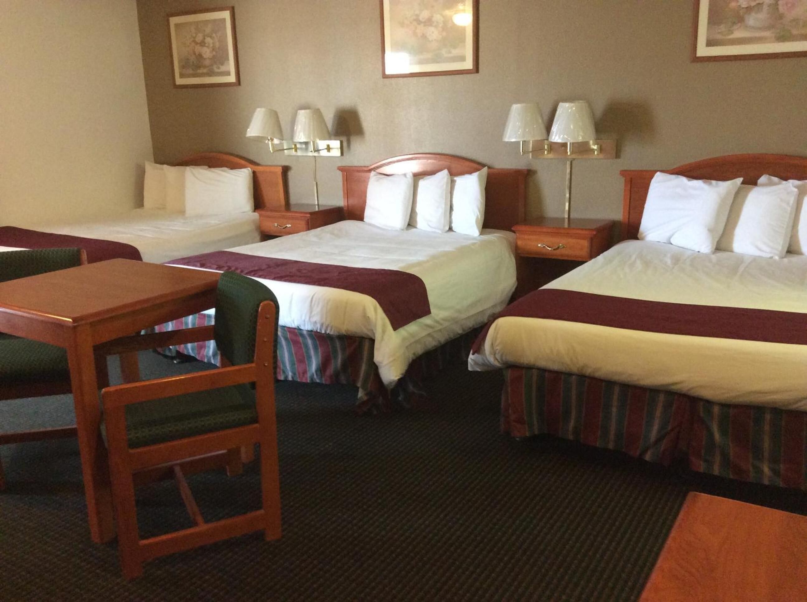 A hotel room with three single beds, a wooden desk, and two chairs.