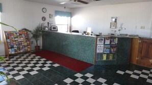 Una zona de recepción con suelo a cuadros, alfombra roja, un mostrador con computadora, un reloj y un tablón de anuncios.