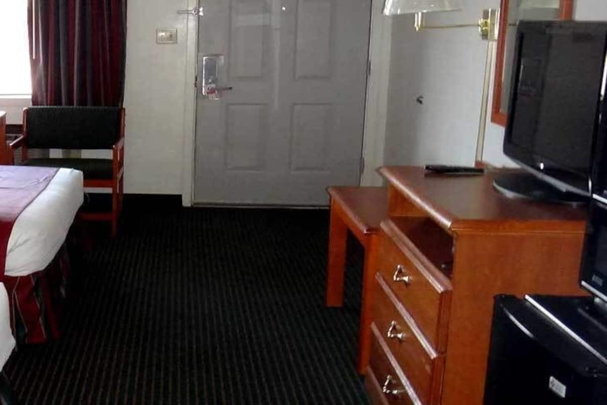 A hotel room with two beds, a desk with a computer, a television, and a door.