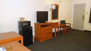 Habitación de hotel con escritorio de madera, televisión, refrigerador, microondas, silla y puerta.