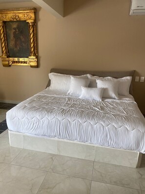 A neatly made bed with white bedding in a room with beige walls and a tiled floor.