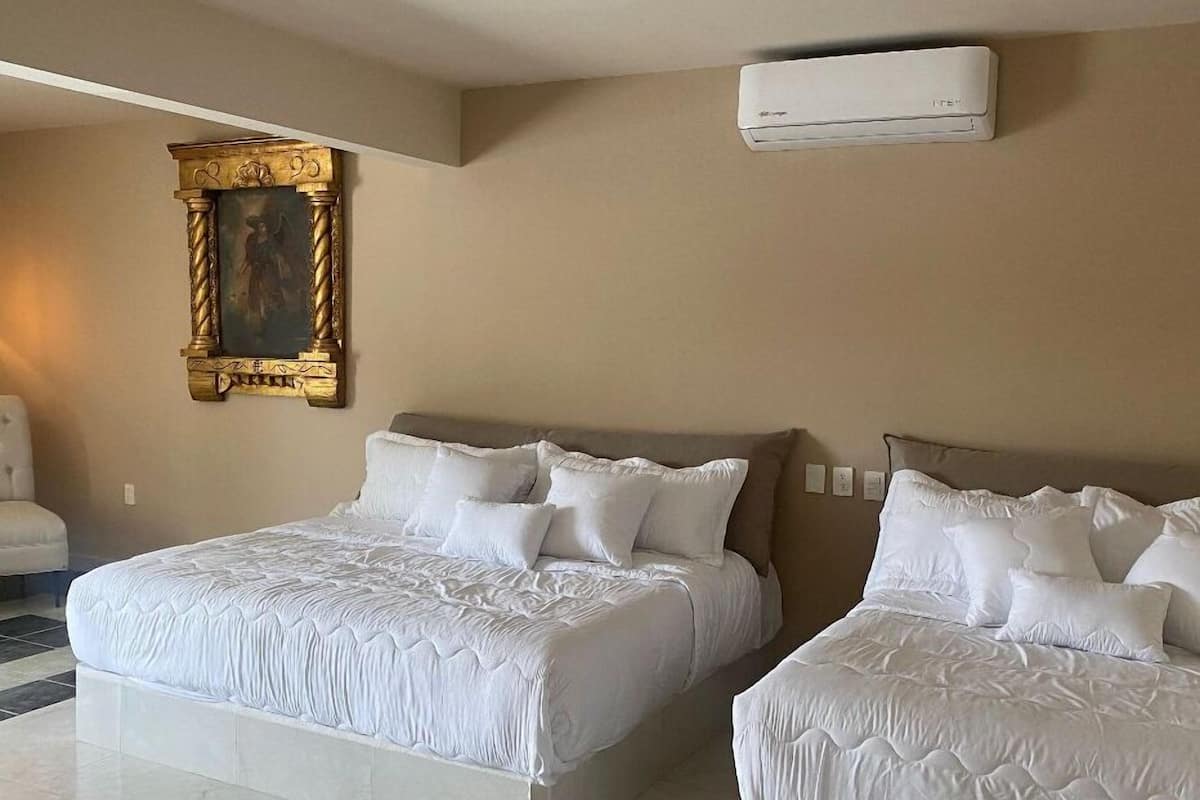 Una habitación de hotel con dos camas, un cuadro en la pared y un equipo de aire acondicionado.
