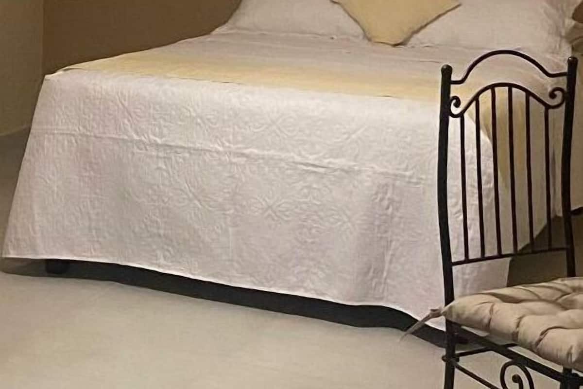 Una cama individual con una colcha blanca y un cabecero, un ventilador de techo y una pared con diseño decorativo.
