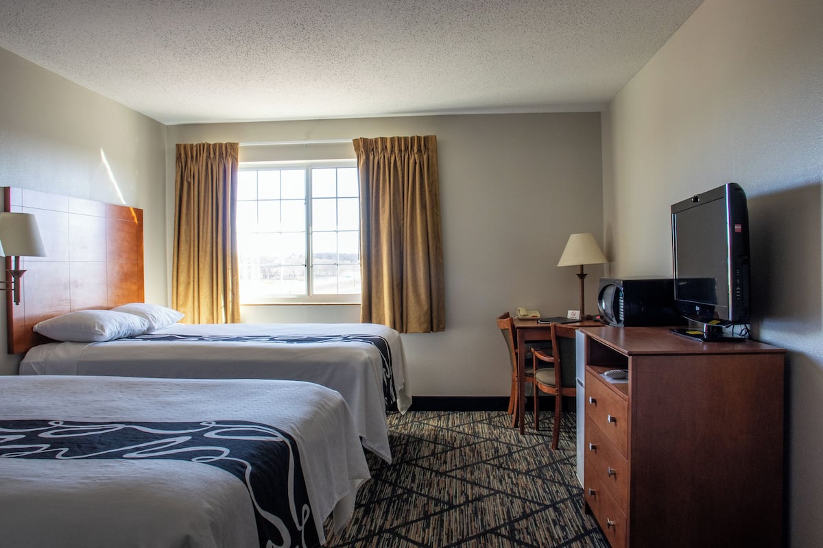 A hotel room with two beds, a desk, a television, and a dresser.