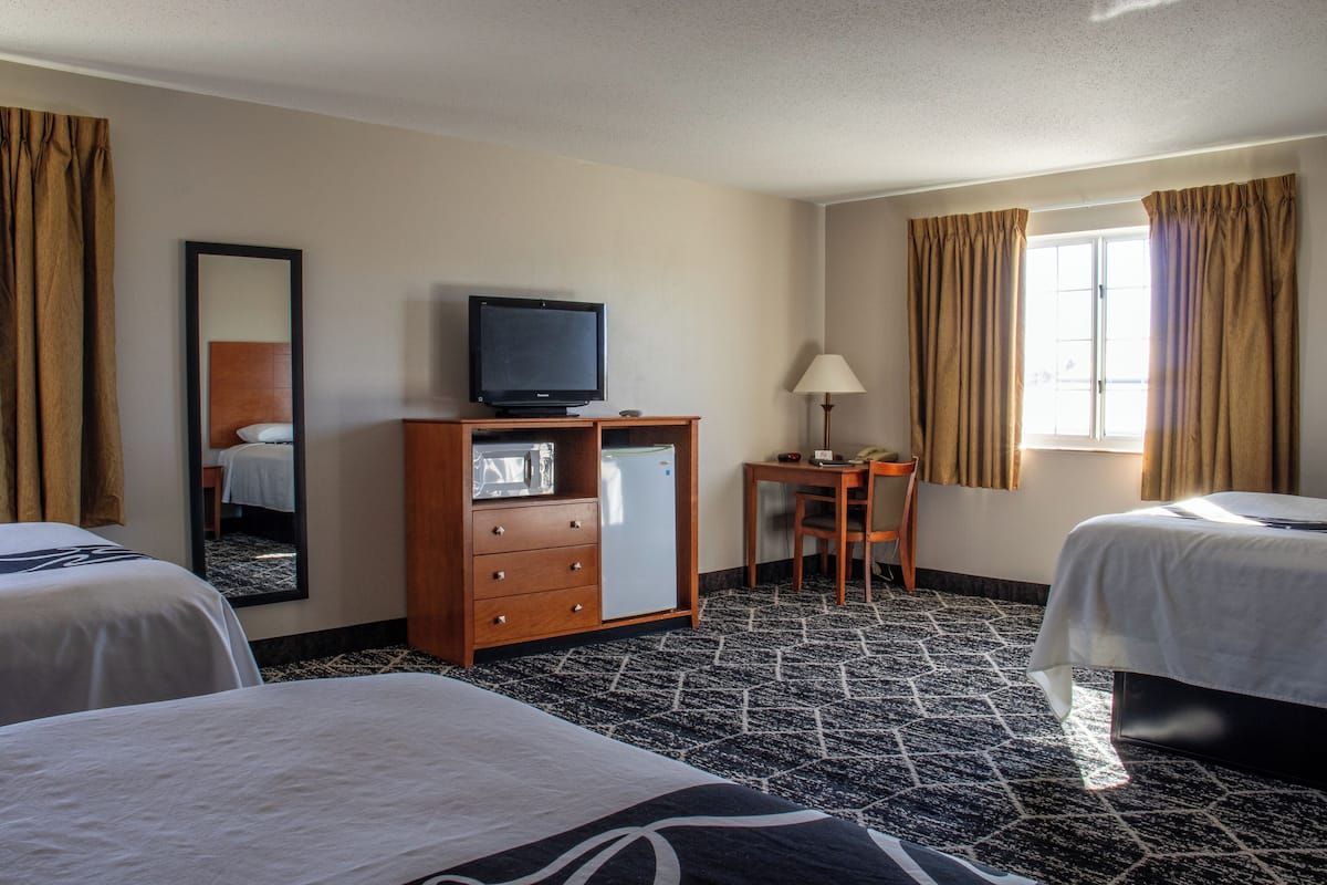 A hotel room with two beds, a television, a desk with a lamp, and a window with curtains.