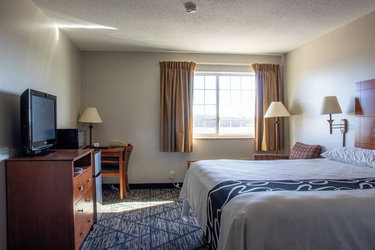 A hotel room with a bed, a desk, a television, two lamps, and a window with curtains.