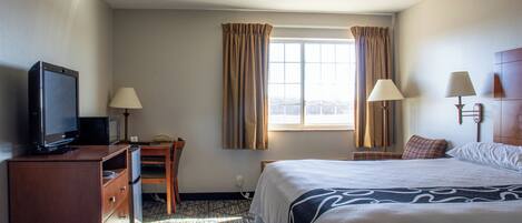 A hotel room with a bed, a desk, a television, two lamps, and a window with curtains.