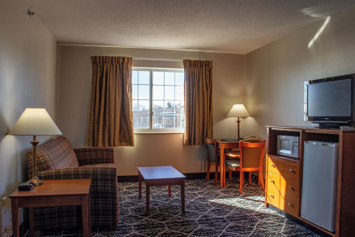 A hotel room with a sofa, two lamps, a television, a small table, and a cabinet.
