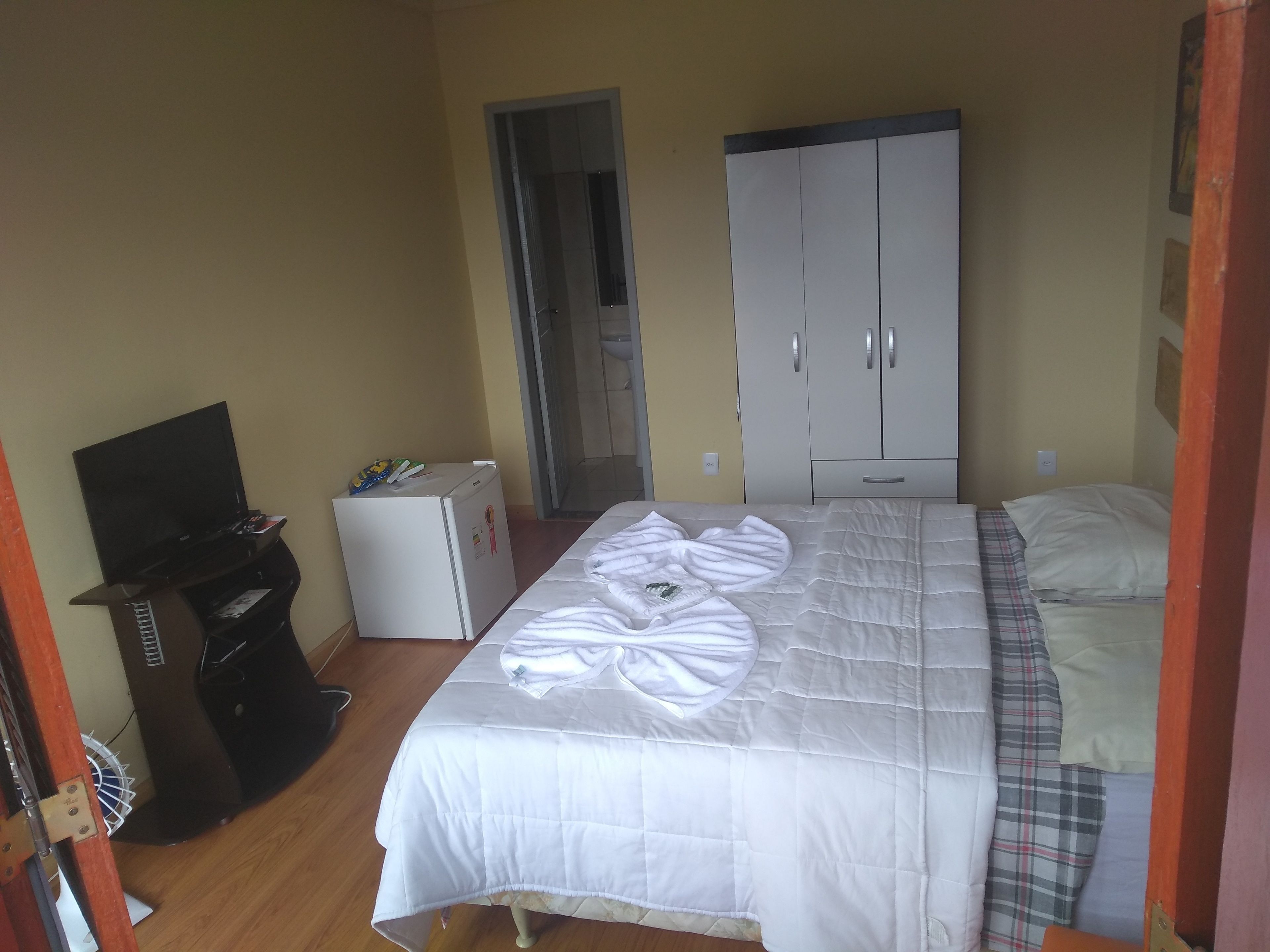 Quarto com cama, guarda-roupa, mini-frigorífico e televisão.