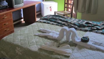 A hotel room with a bed, a wooden desk with drawers, a television, and a refrigerator.