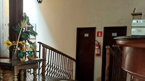 Vestíbulo de hotel con una escalera de madera, un extintor y una olla de cobre grande sobre una mesa.