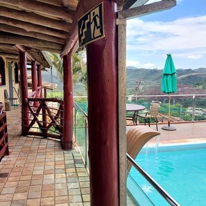 Ein überdachter Außenbereich mit Pool, Holzmöbeln und Blick auf die Landschaft.