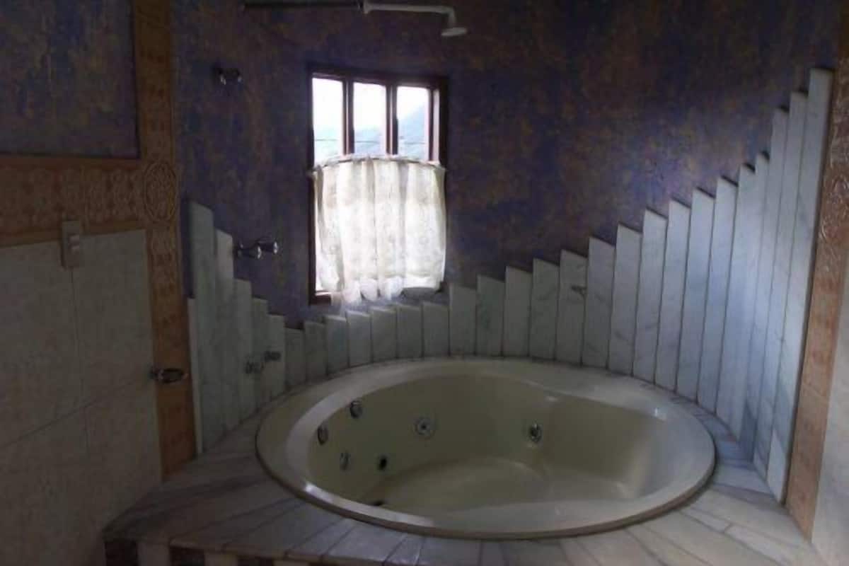 A large, empty bathtub in a room with a sloped ceiling and a window with curtains.