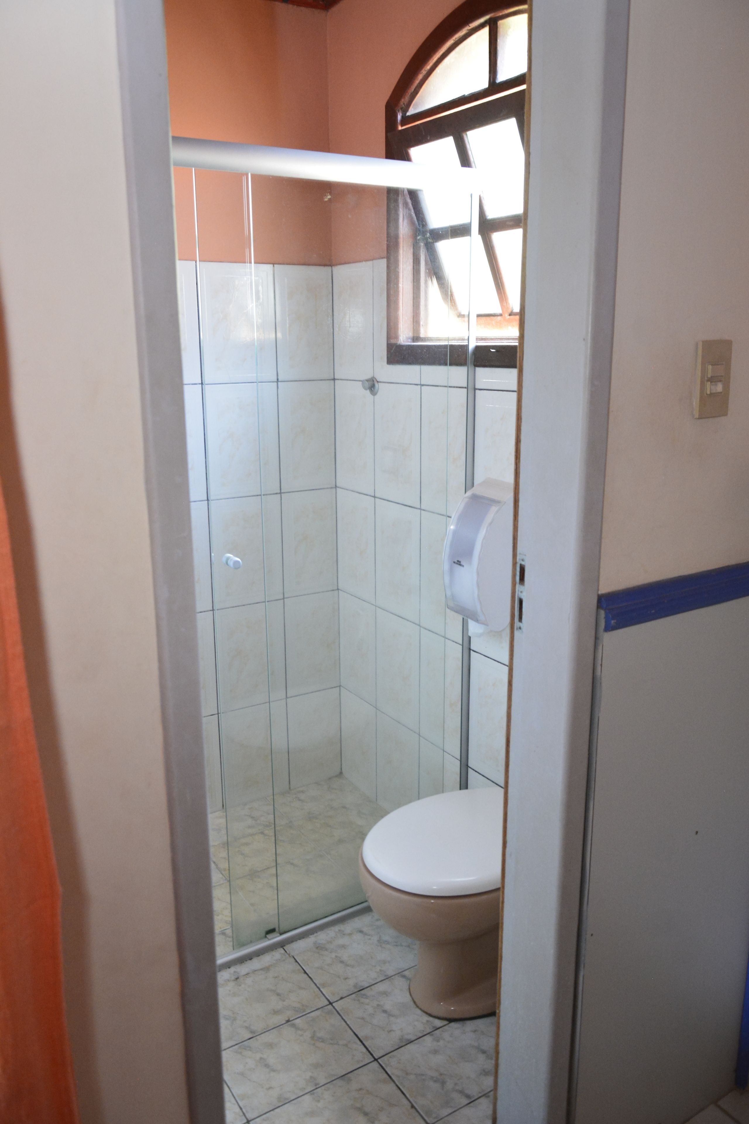 A small bathroom with a toilet, a glass shower enclosure, and a window above the toilet.