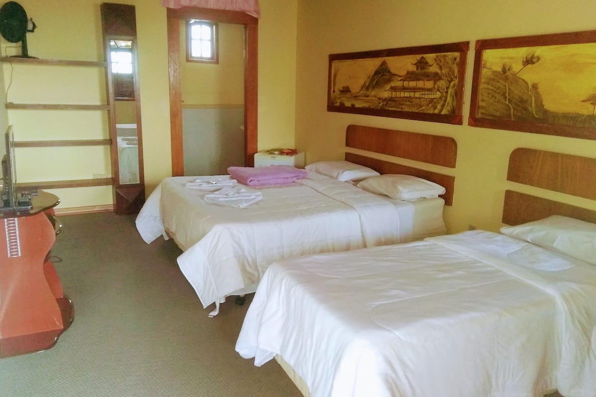 A hotel room with two beds, a desk, a mirror, and artwork on the wall.