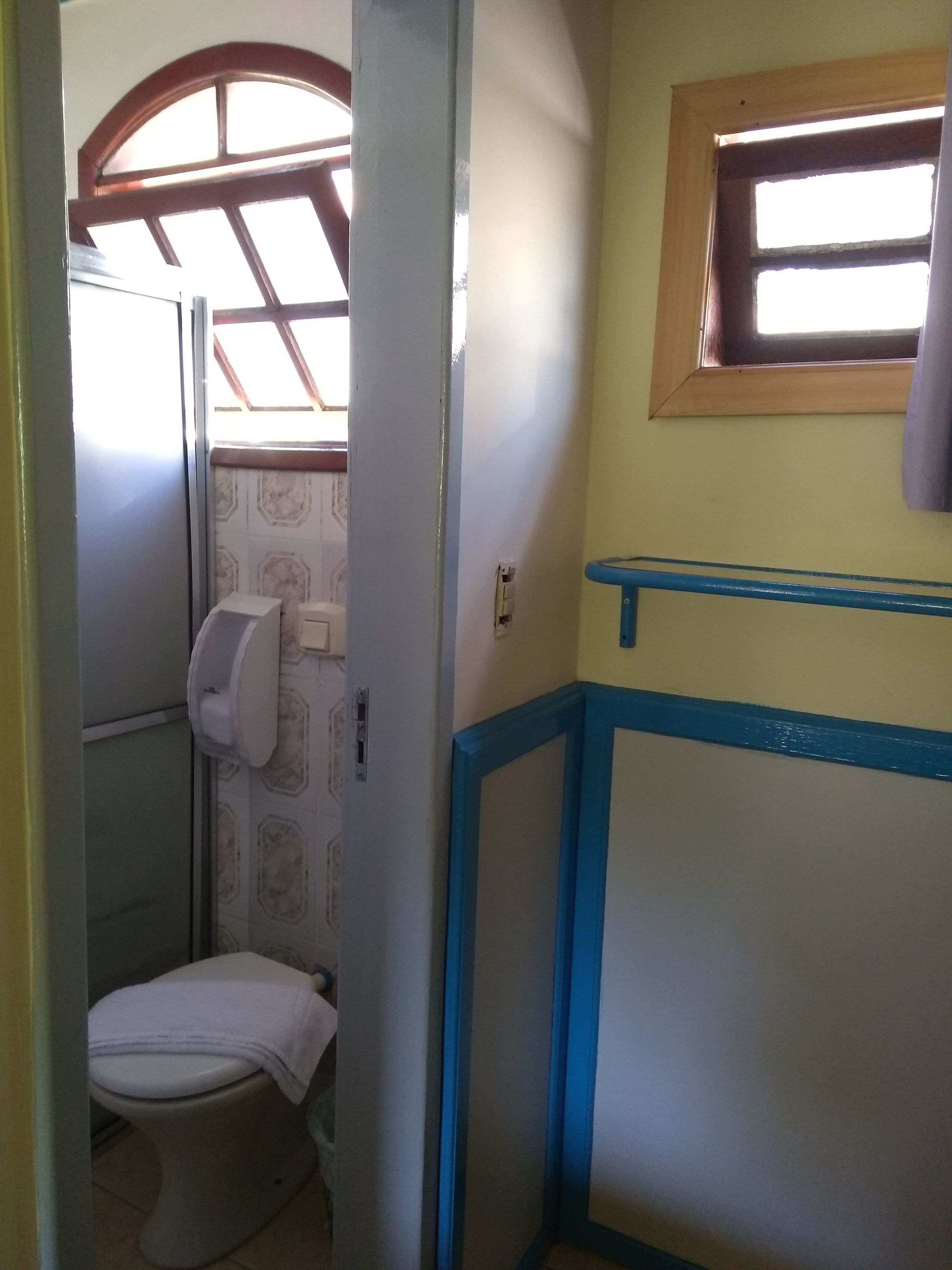 Ein kleines Badezimmer mit Toilette, Handtuchspender und einem Fenster mit Holzrahmen.