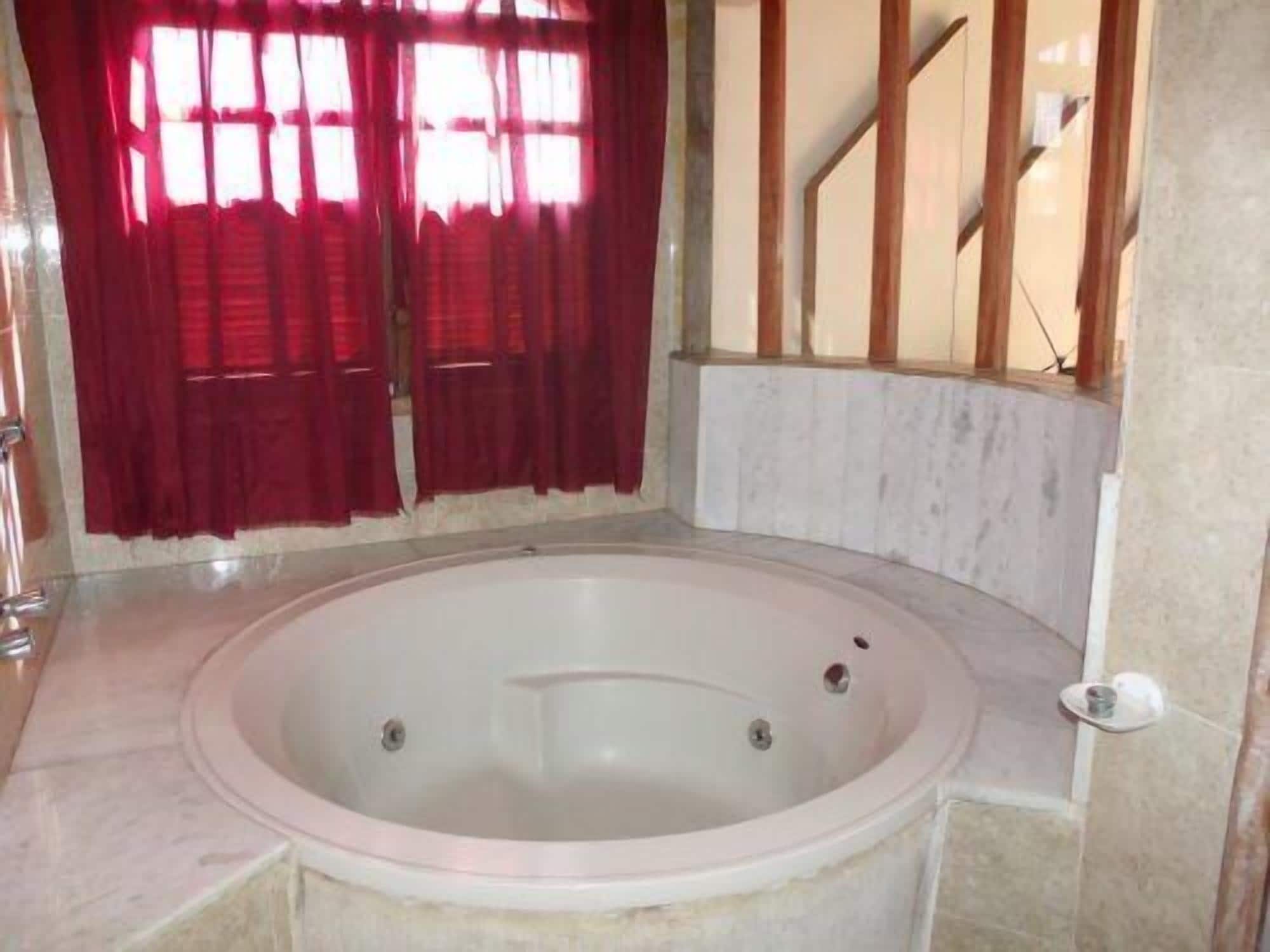 A bathroom with a large bathtub, a window with red curtains, and a marble floor.