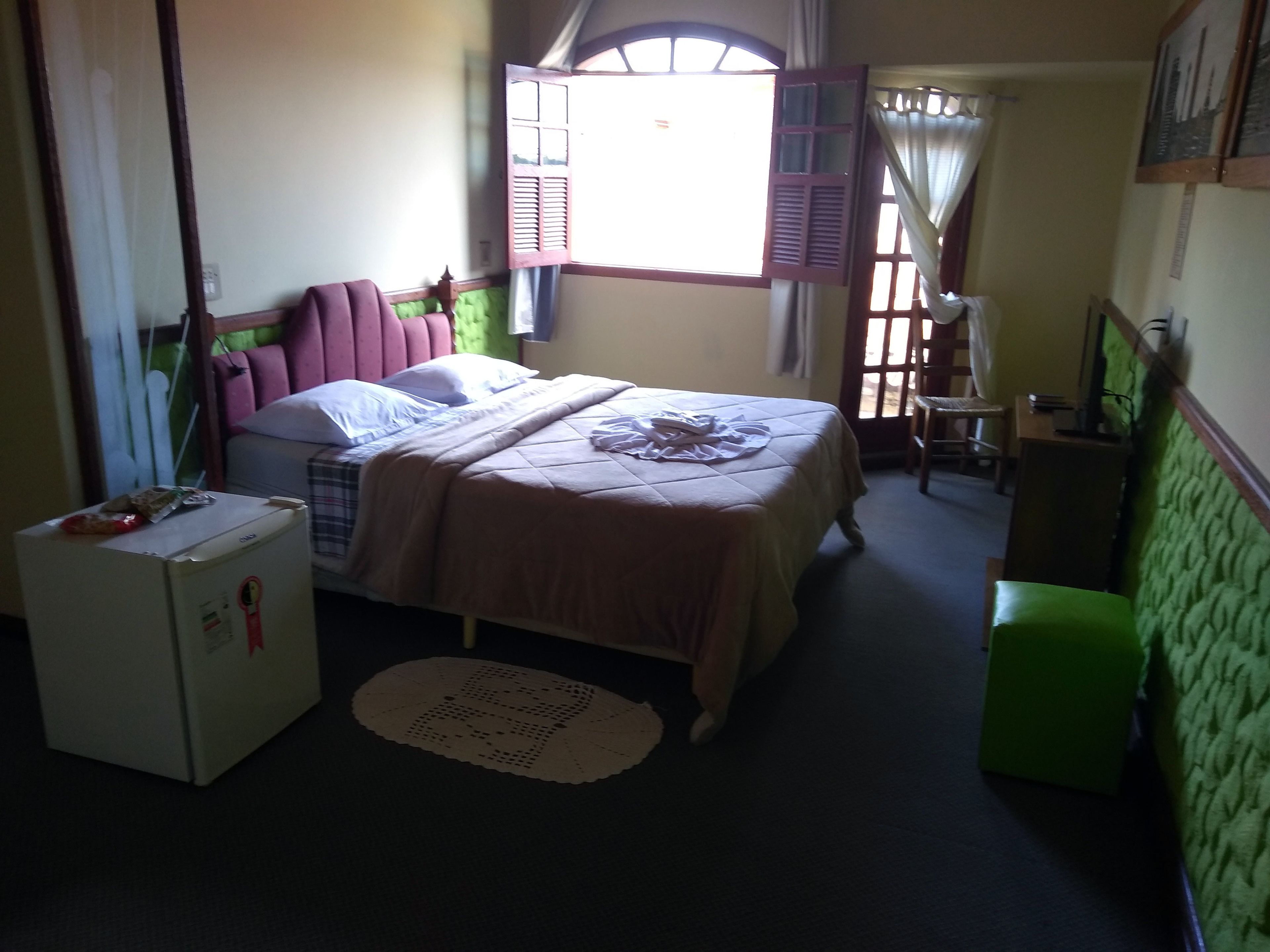 A small, cozy room with a bed, a desk, a chair, and a refrigerator.