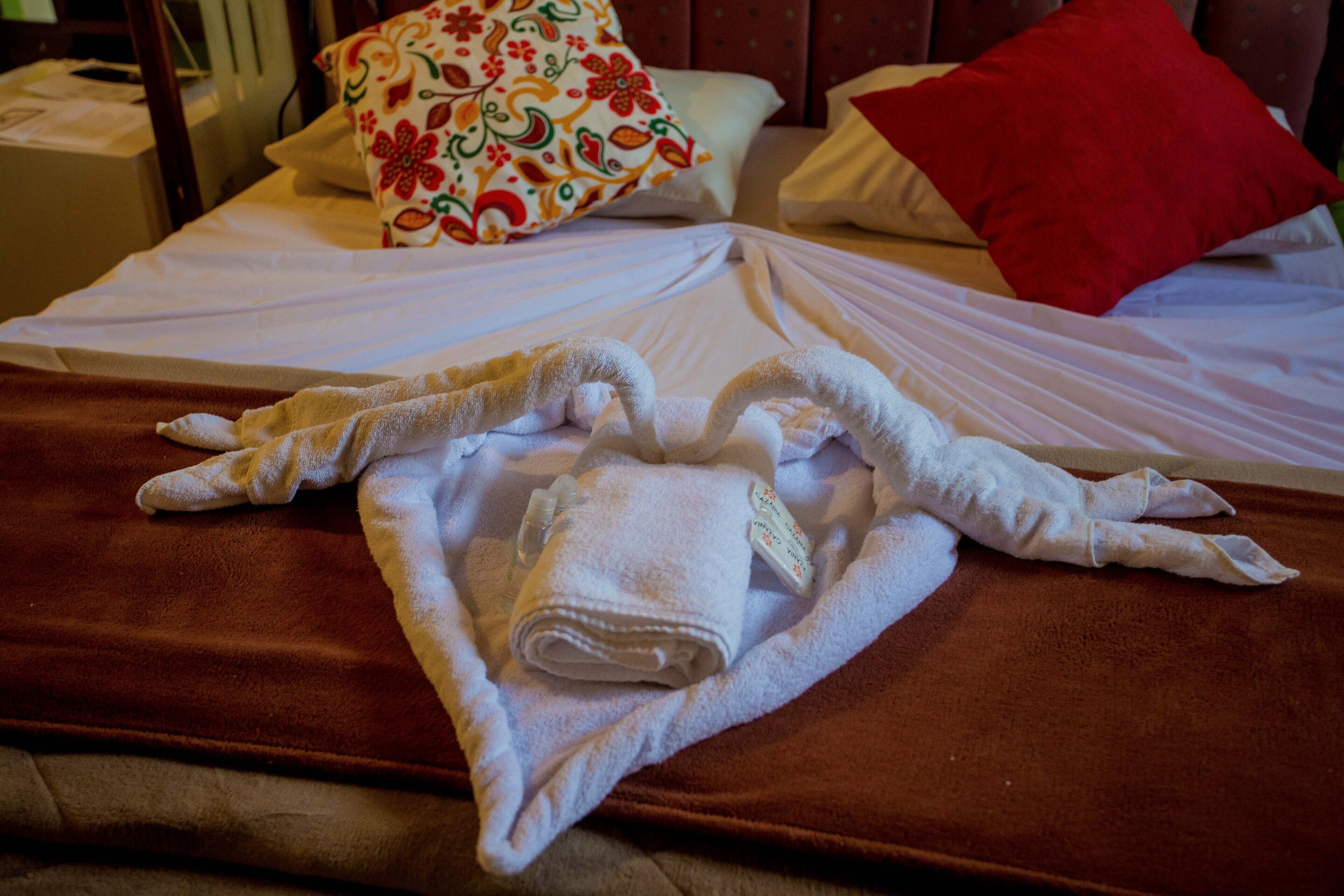 A neatly made bed with a brown bedspread, white linens, and a rolled-up towel with a tag.