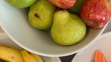 A bowl of green pears and red apples, a plate of bananas, and a bowl of sliced carrots.