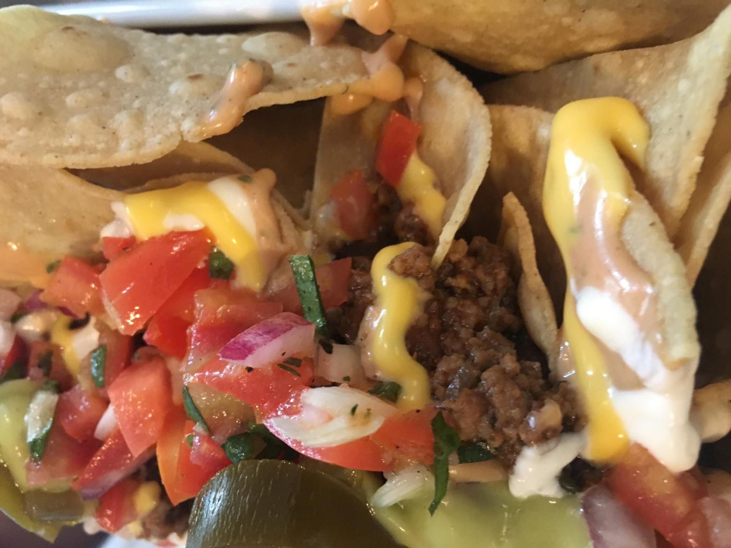 A close-up of a taco dish with ground meat, diced tomatoes, onions, and a creamy sauce.