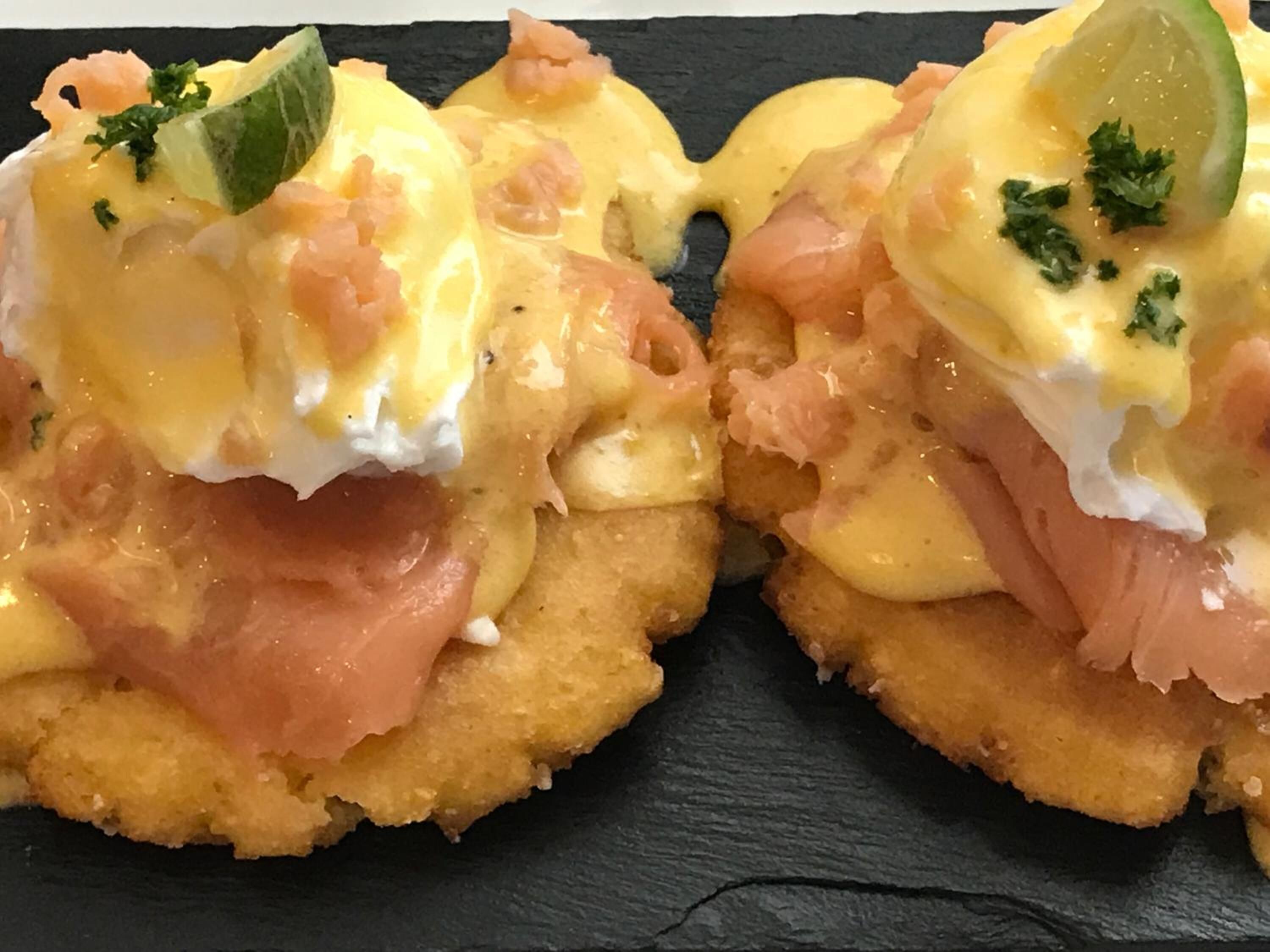 Two eggs benedict sandwiches on a black slate plate.