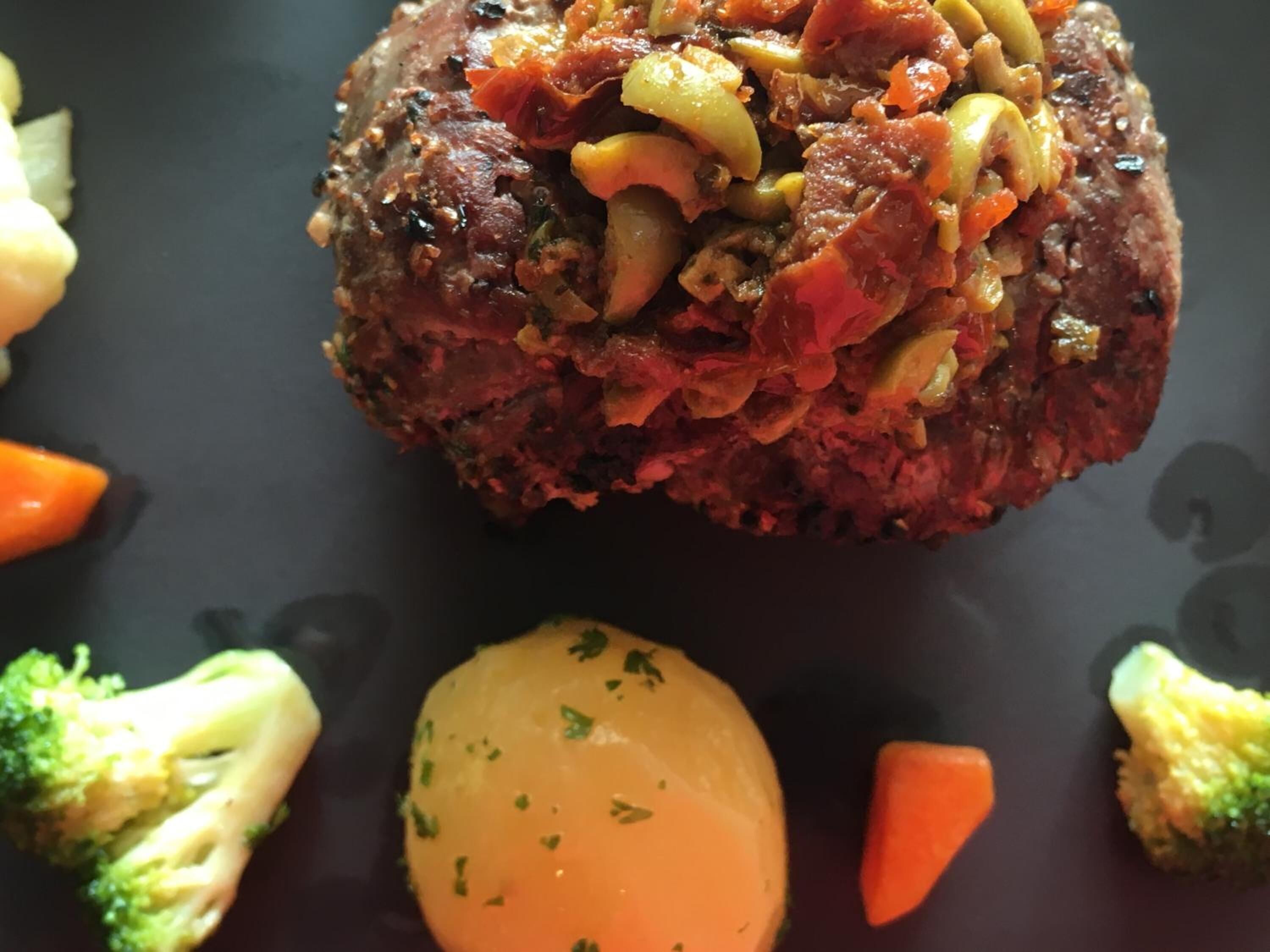 A steak topped with vegetables and surrounded by broccoli and carrots.