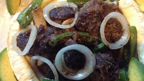 Plato con carne, cebollas y pimientos verdes sobre pan plano.