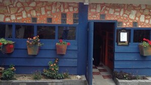 Un edificio con fachada de piedra y paredes exteriores azules. Hay macetas con plantas en los alféizares de las ventanas.