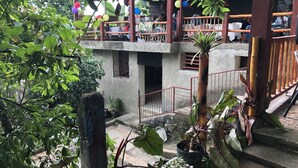 Un espacio al aire libre cubierto con una estructura de concreto, plantas en macetas y una barandilla metálica.