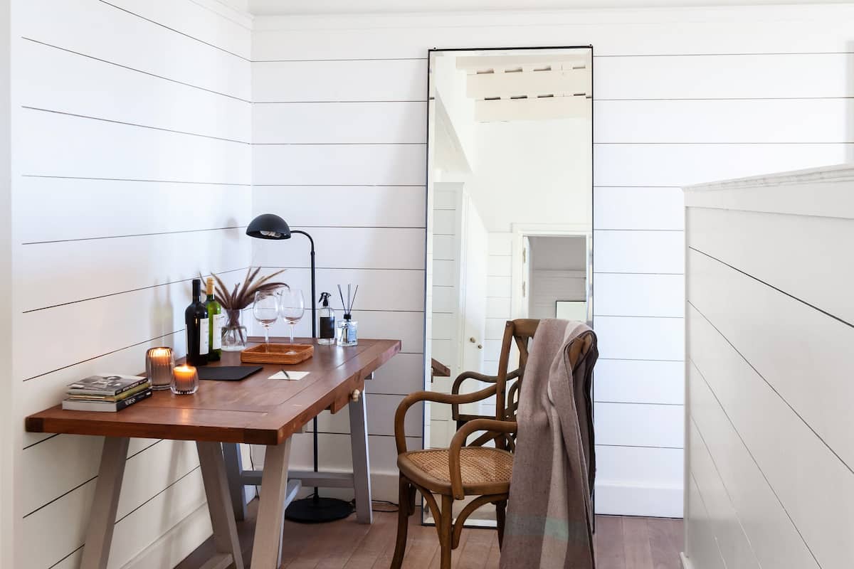 A small, cozy room with a wooden desk, a chair, a mirror, and a patterned rug.