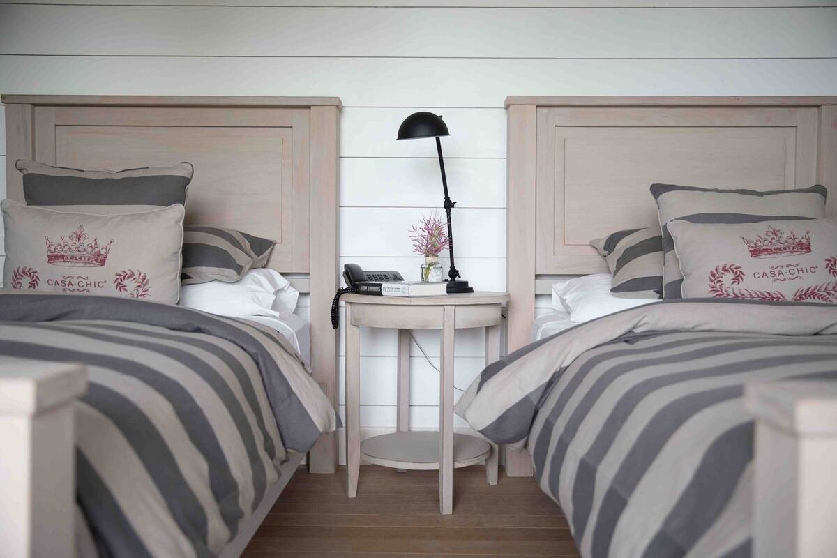 A bedroom with two beds, a bedside table, a lamp, and a vase with flowers.