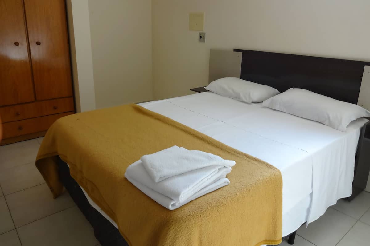 A hotel room with a bed, a wooden wardrobe, and a wall socket.