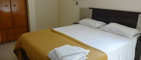 A hotel room with a bed, a wooden wardrobe, and a wall socket.