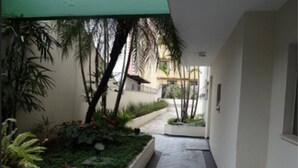 Un couloir étroit, agrémenté de jardinières contenant diverses plantes et fleurs, qui mène à l’entrée d’un bâtiment.